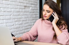 A woman makes a phone call while using a laptop.